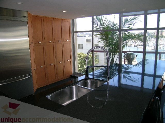 Bright kitchen with black countertops and a city view, featuring stainless steel appliances and wooden cabinets. - 310 - 990 Beach, Vancouver Downtown