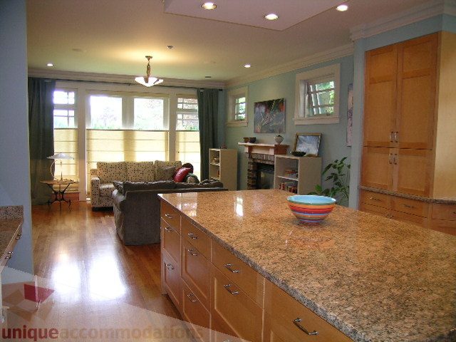 Bright kitchen with granite countertops and hardwood floors, leading to a cozy living area with large windows.
