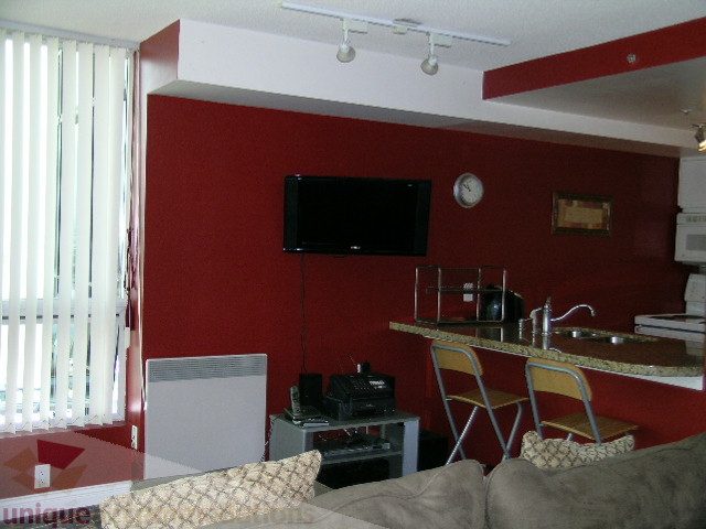 Furnished living room with red walls, built-in TV, and small dining area with bar stools. - 1403 - 555 Jervis Street, Vancouver Downtown