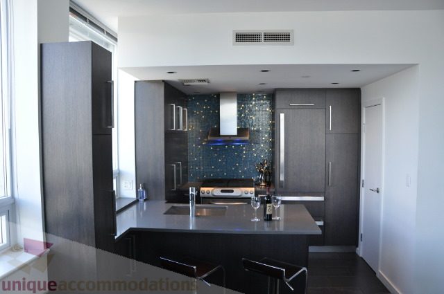 Bright kitchen with modern dark wood cabinets, glass mosaic backsplash, and stainless steel appliances.