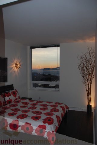 Furnished bedroom with red floral bedding and city view at sunset. - 2702 - 638 Beach Crescent, Vancouver Downtown