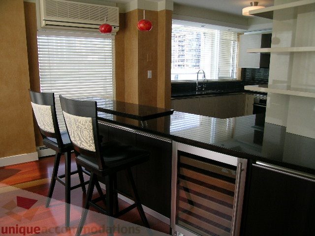 Bright kitchen with modern black countertops and wooden bar stools, featuring a city view through large windows.
