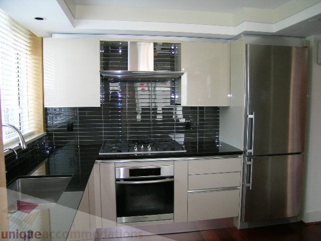 Bright kitchen with modern stainless steel appliances, black tile backsplash, and hardwood floors.