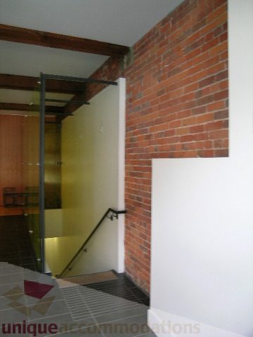 Bright hallway with exposed brick wall and black handrail leading to stairs. - 902 - 528 Beatty Street, Vancouver Downtown