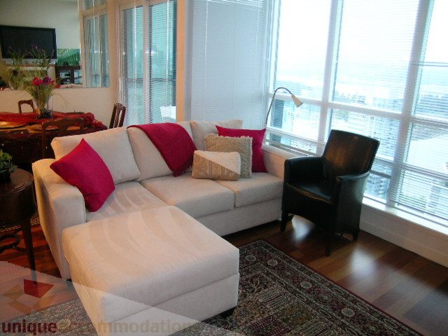 Bright living room with white sectional sofa, hardwood floors, and city view. - 3802 - 1189 Melville Street, Vancouver Downtown