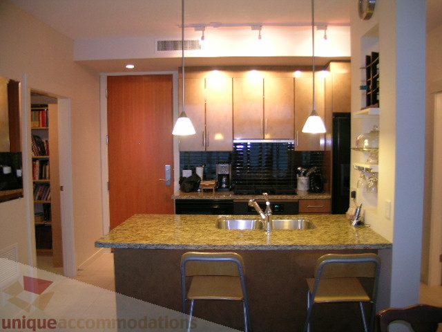 Bright kitchen with granite countertops and modern appliances, featuring a breakfast bar with two stools.