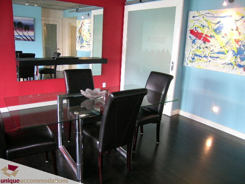 Modern dining area with glass tables, black chairs, red and blue walls, and vibrant abstract art. - 705 - 1500 Howe street, Vancouver Downtown