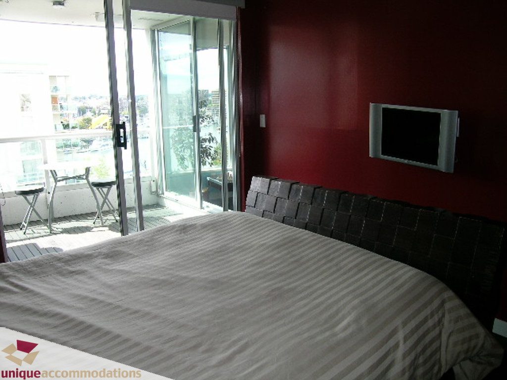 Spacious bedroom with a large bed, red accent wall, and sliding glass doors offering a city view. - 705 - 1500 Howe street, Vancouver Downtown
