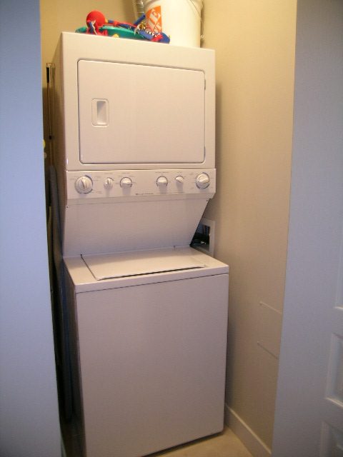 Bright laundry room with stacked washer and dryer, white walls, and a small storage area above. - 315 - 4078 Knight Street, Vancouver West Side