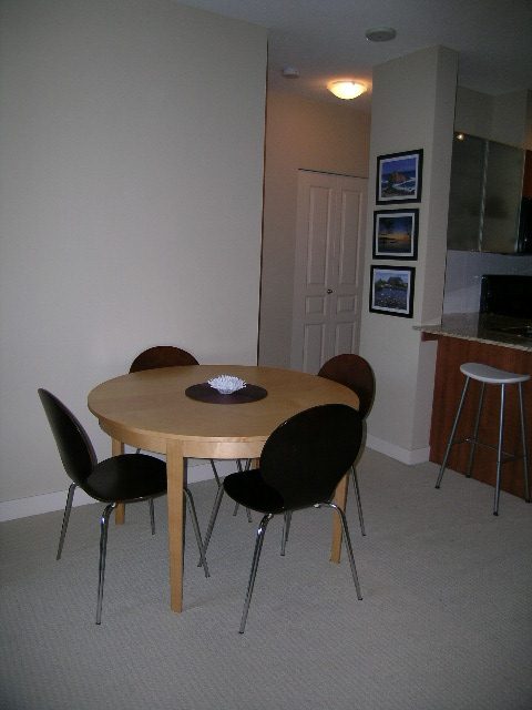 Bright dining area with wooden tables and chairs, light-colored walls, and a kitchen counter in the background.
