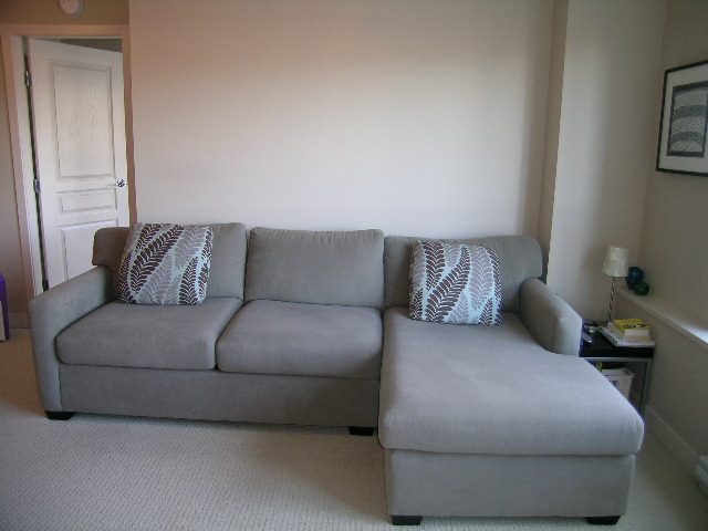 Bright living room with a sectional sofa, neutral decor, and a small side table. - 315 - 4078 Knight Street, Vancouver West Side