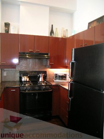 Bright kitchen with dark cabinetry, stainless steel appliances, and a black countertop. - 208 - 428 West 8th Ave, Vancouver West Side