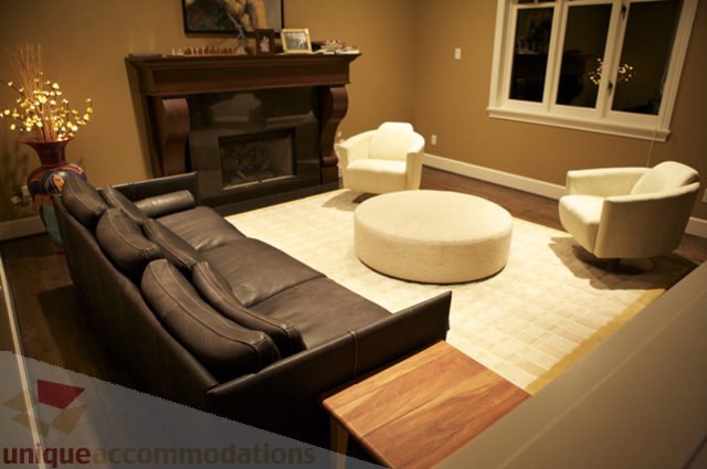 Furnished living room with a cozy fireplace, plush seating, and a large ottoman. - 3781 Bayridge Ave, West Vancouver