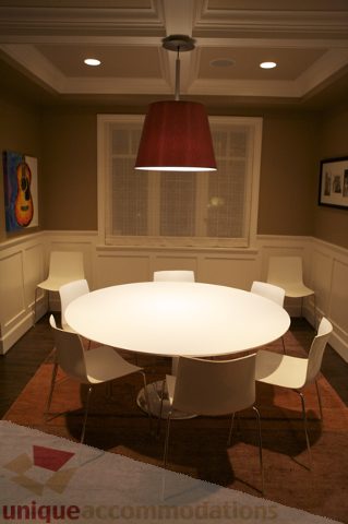 Dining area with modern white table, red pendant light, and wainscoting. - 3781 Bayridge Ave, West Vancouver