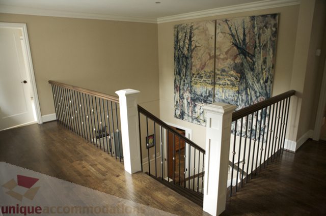 Staircase with wooden railings and large artwork on the wall. - 3781 Bayridge Ave, West Vancouver