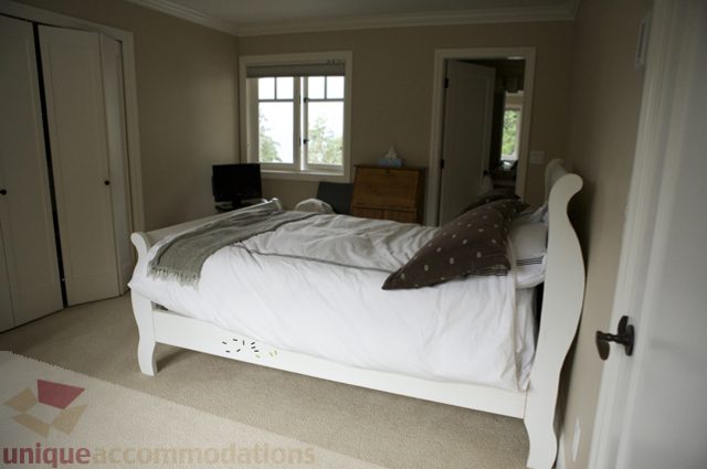 Spacious bedroom with white sleigh bed, beige walls, and natural light from window. - 3781 Bayridge Ave, West Vancouver