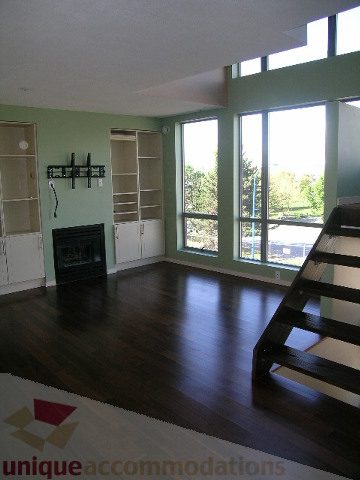 Spacious living room with hardwood floors, large windows, and a cozy fireplace. - 137 Alexander Street, Vancouver Downtown