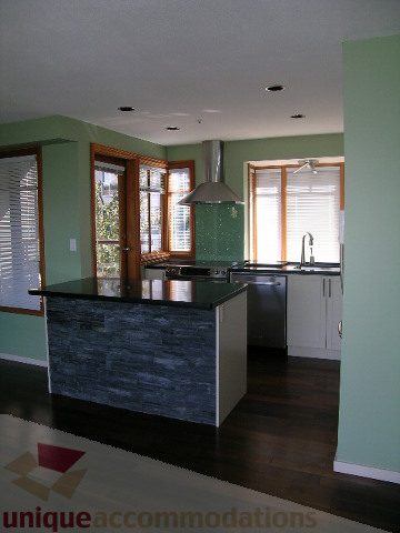Bright kitchen with dark stone countertops and hardwood floors, featuring a city view through large windows.