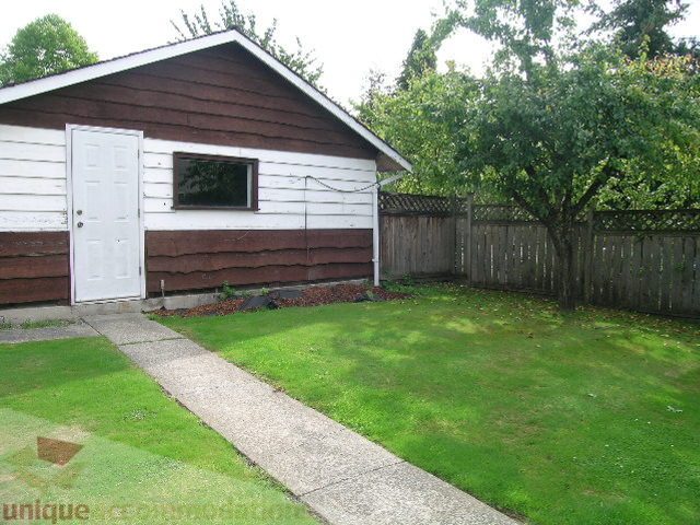 Bright backyard with green lawn and wooden fence, leading to a brown and white house with a small window and door.