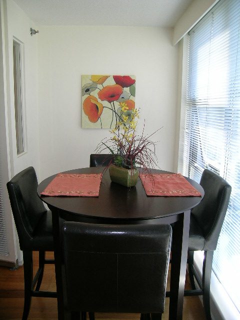 Dining area with black leather chairs, round table, red placemats, and floral artwork. - 1102 - 1723 Alberni Street, Vancouver Downtown