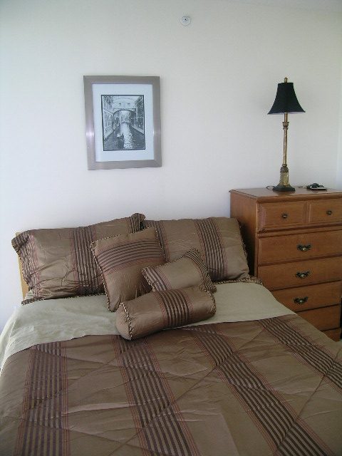 Bedroom with neatly made bed, wooden dresser, and framed artwork on the wall. - 1102 - 1723 Alberni Street, Vancouver Downtown