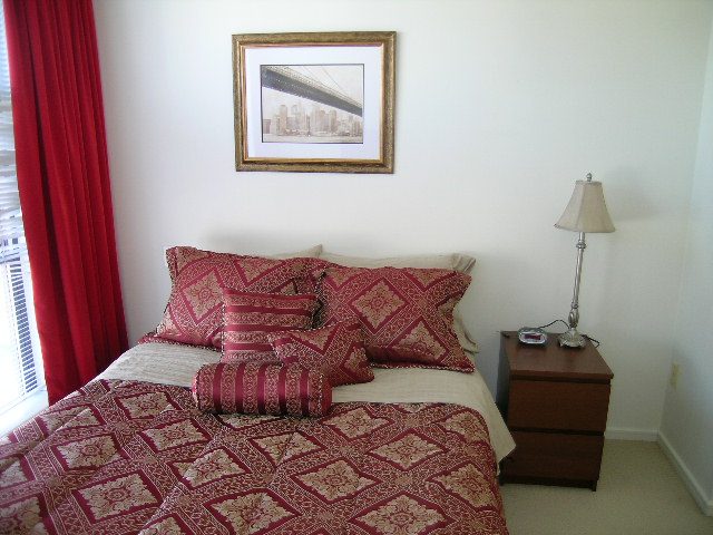 Bright bedroom with red and white patterned bedding, cityscape artwork, and red curtains. - 1102 - 1723 Alberni Street, Vancouver Downtown