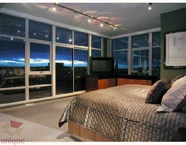 Spacious bedroom with large windows offering a stunning city view, modern furnishings, and a cozy ambiance.