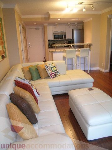 Spacious living room with white leather sectional, hardwood floors, and modern kitchen counter. - 1205 - 1331 West Georgia Street, Vancouver Downtown