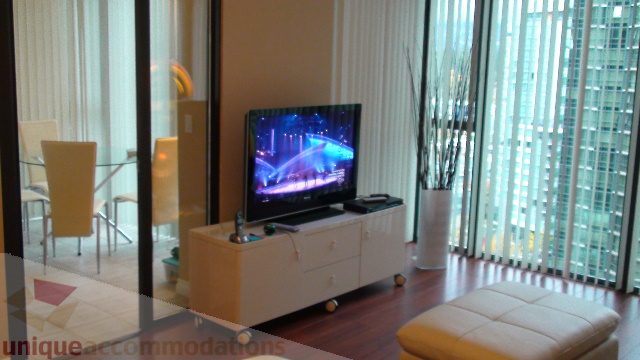Spacious living room with hardwood floors, a large TV, and a city view. - 1205 - 1331 West Georgia Street, Vancouver Downtown