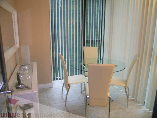 Spacious dining area with modern glass table and sleek white chairs, offering a view of the city skyline.