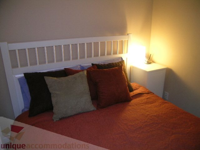 Cozy bedroom with a warm, inviting ambiance, featuring a neatly made bed with red bedding and a white headboard, and a...