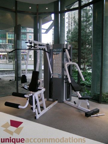 Spacious living room with large windows offering a stunning city view and modern fitness equipment.