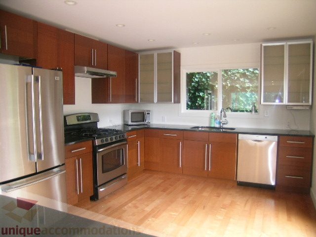 Bright kitchen with stainless steel appliances, hardwood floors, and a city view through the window. - 250 Rockland Road West, North Vancouver