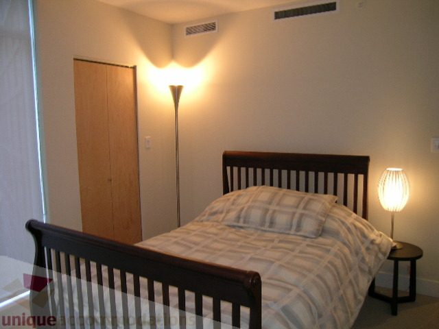Furnished bedroom with wooden bed frame and modern lighting fixtures. - 604 - 1205 West Hastings Street, Vancouver Downtown