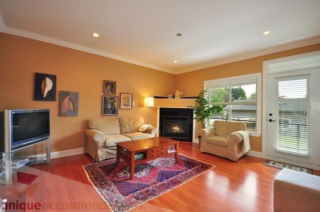 Furnished living room with hardwood floors, large windows, and a cozy fireplace. - 341 East 8th Street, North Vancouver