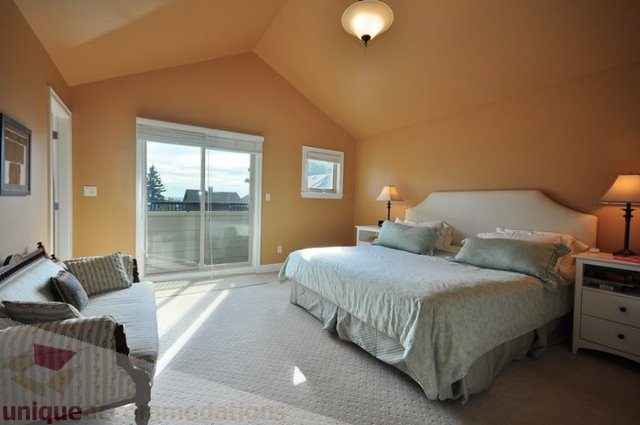 Spacious bedroom with vaulted ceiling, large window, and cozy bedding. - 341 East 8th Street, North Vancouver