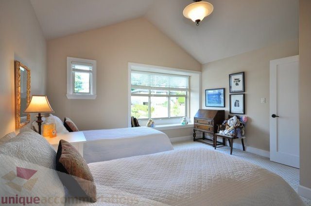 Spacious bedroom with large windows, cozy bedding, and a lamp. - 341 East 8th Street, North Vancouver