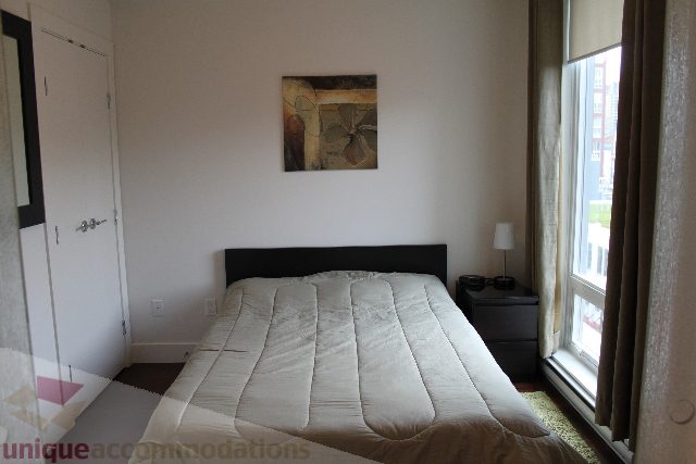 Furnished 1-bedroom with a cozy bed, large window, and abstract wall art. - 705 - 565 Smithe Street, Vancouver Downtown