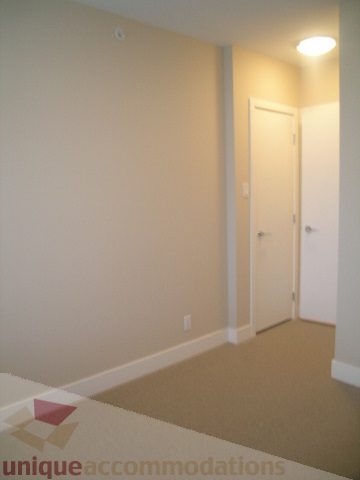 Spacious living room with neutral walls, carpeted floor, and access to another room. - 1309 Civic Place Mews, North Vancouver