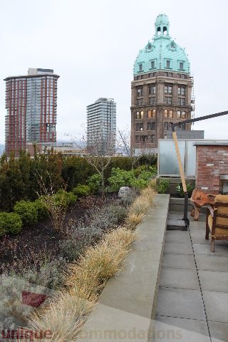 Furnished rooftop patio with city view and garden, featuring stone pavers and outdoor seating. - 701 - 546 Beatty Street, Vancouver Downtown