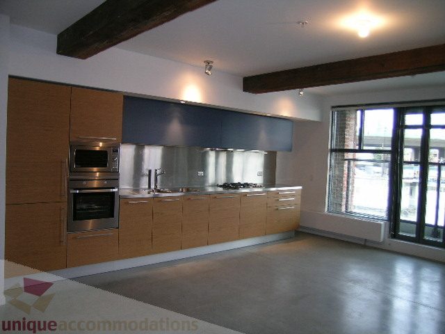 Bright kitchen with modern appliances, wooden cabinets, and large windows offering city views. - 216 - 388 West 1st Avenue, Vancouver West Side