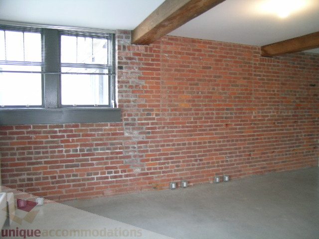 Exposed brick wall with concrete floor and wooden beams. - 216 - 388 West 1st Avenue, Vancouver West Side