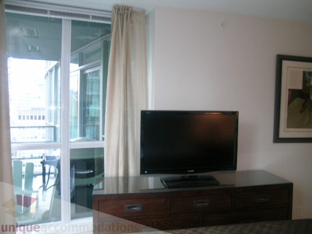 Furnished living room with glass-top desk, city view, and large windows. - 907 - 1189 Melville Street, Vancouver Downtown