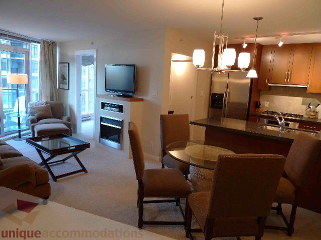 Spacious open-concept living area with modern furnishings, city view, and stainless steel appliances. - 907 - 1189 Melville Street, Vancouver Downtown