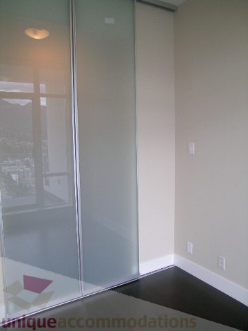 Spacious bedroom with frosted glass sliding doors and a city view. - 1903 - 1320 Chesterfield Street, North Vancouver