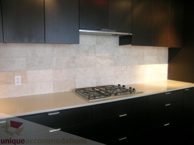 Modern kitchen with sleek black cabinets, white tile backsplash, and stainless steel appliances. - 1903 - 1320 Chesterfield Street, North Vancouver