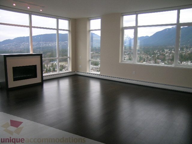 Spacious living room with hardwood floors, large windows offering a stunning city view, and a modern fireplace.