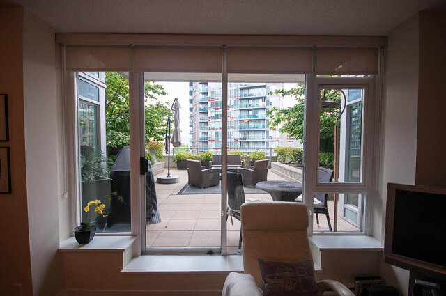 Spacious living room with large sliding glass doors opening to a cozy patio, featuring outdoor furniture and a city view.