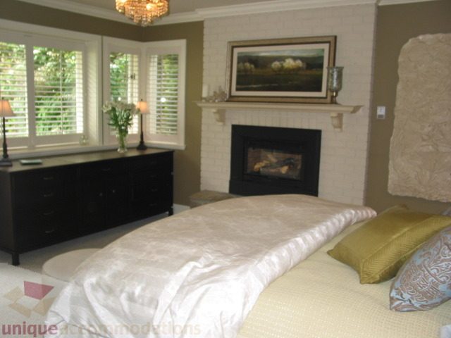 Spacious bedroom with a cozy fireplace, white bedding, and a view of greenery outside. - 1330 Sinclair Street, West Vancouver