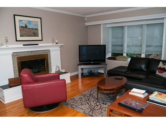 Spacious living room with hardwood floors, a red leather chair, and a fireplace. - 5680 Marine Drive, West Vancouver